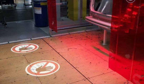 Proyección de señal de seguridad en el suelo de una fábrica, indicando prohibición de acceso con un símbolo de mano y un círculo rojo.